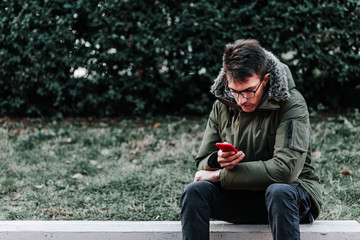 Obraz premium Young man sitting outdoors using his smartphone