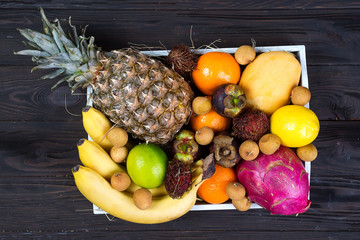 Fototapeta na wymiar Fresh exotic fruits in a wooden box, top view with many colorful ripe fruits