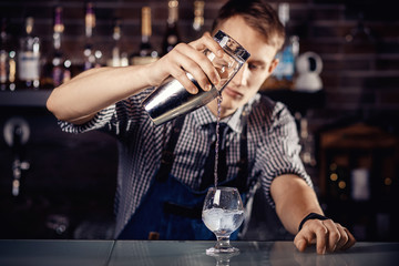 Barman prepares cocktail in shaker with alcohol and ice. Dark background Bartender
