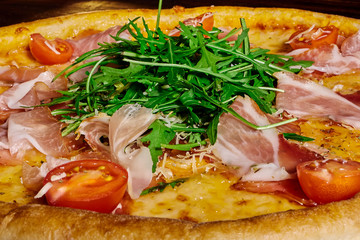 Fototapeta na wymiar Italian pizza with ham, tomatoes and herbs on a wooden table ?lose up