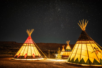 Illuminated Native American Teepees under glowing night sky
