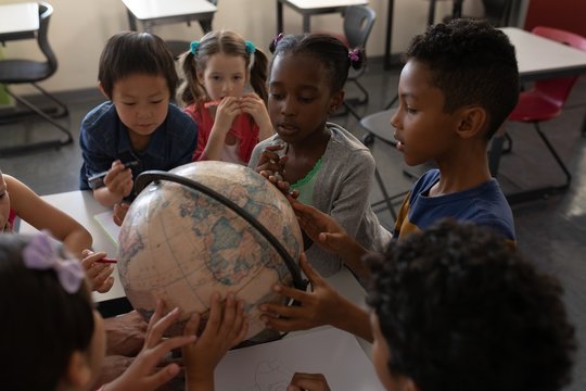 Group of kids studying a globe together in classroom