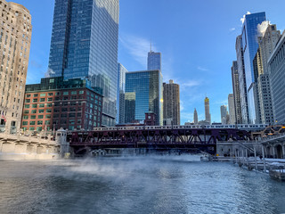 Elevated train crosses a freezing Chicago River as steam rises while temperatures plummet