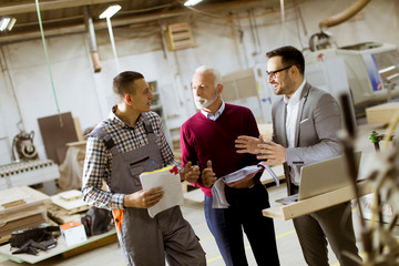 Three men standing and discuss in furniture factory