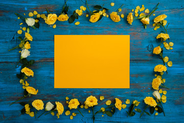 The composition of flowers. Frame made of yellow flowers on a blue wooden background. Easter, spring, summer concept. Flat lay, top view.