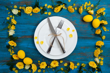 Easter table setting on blue wooden background with yellow spring flowers and eggs.