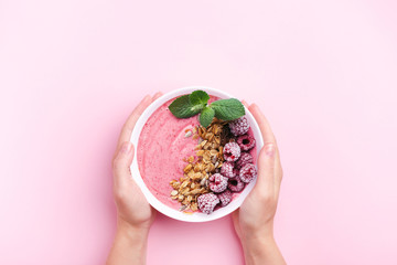 Woman's hands holding raspberries smoothie bowl with mint leaf on pink background. Top view, copy...