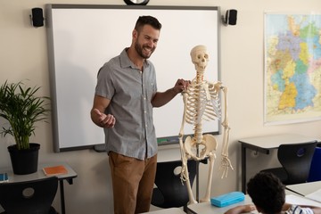 Side view of happy male teacher explaining human skeleton model