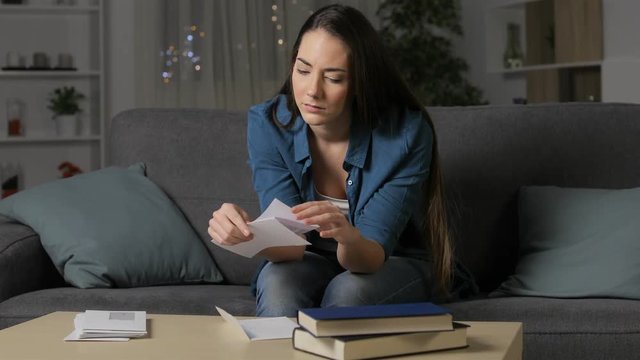 Angry woman reading a letter in the night sitting on a couch in the living room at home