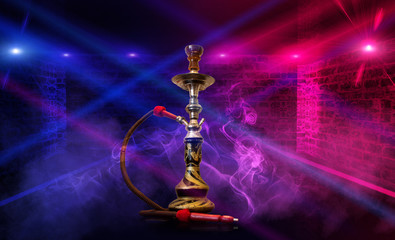 Smoking hookah on the background of an empty room. Multicolored neon light. Searchlight, laser blue and pink rays, smoke.