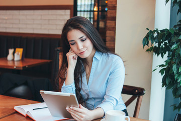 Beautiful charming brunette sad Asian girl working or studying at table in cafe, student, freelancer