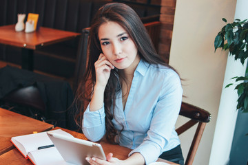 Beautiful charming brunette sad Asian girl working or studying at table in cafe, student, freelancer