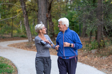 Active senior couple jogging in the park at autumng day and smile