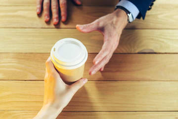 Barista serves coffee to a man. Hand Paper cup Plastic cap Wooden table Break Blazer. Coffee Break Concept