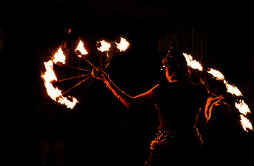 fire-eater, fire dancer with flaming hoop in night show at medieval festival with black background,...