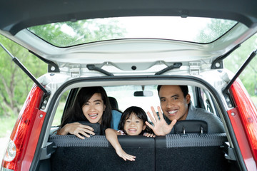 mother, father, and his daughter inside a car look out from back windows