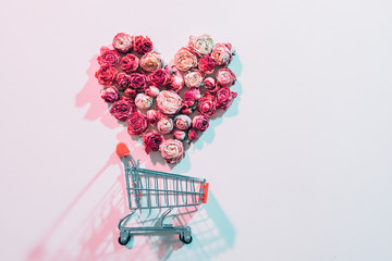 Valentines day shopping. Flower love shaped heart falling into empty trolley. Pink background.