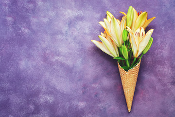 Yellow lilies in a waffle cone on abstract purple background. Beautiful spring creative background, place for text.
