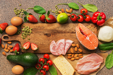 Healthy foods low in carbohydrates. Keto diet concept. Salmon, chicken, vegetables, strawberries, nuts, eggs and tomatoes, cutting board. Healthy foods low in carbohydrates. Top view.