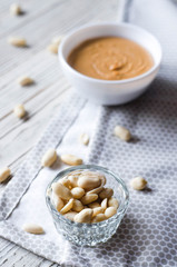 Appetizing peanuts with a plate of peanut butter on a light background.