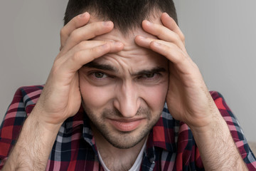 A male has a headache, squeezes his head with his hands, close up