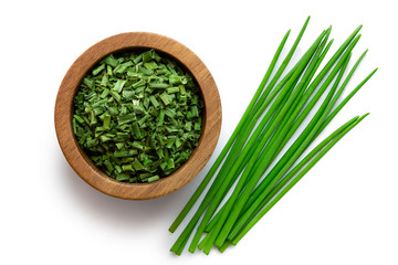 Dried chopped chives in a dark wood bowl next to a pile of whole fresh chives isolated on white...
