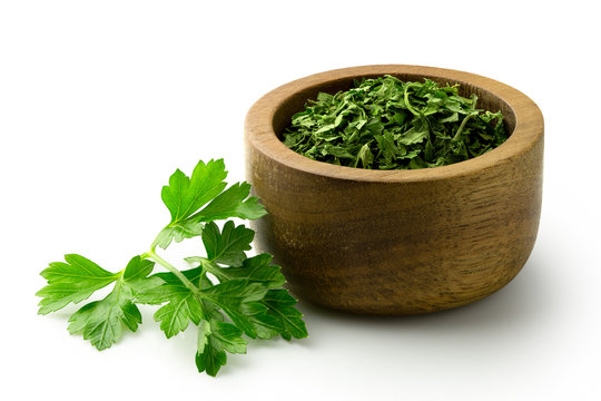 Dried chopped parsley in dark wood bowl next to fresh parsley leaves isolated on white.
