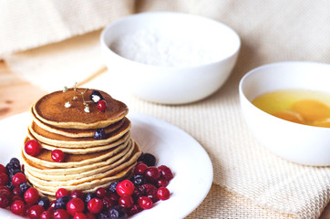 A stack of pancakes with blueberries and cranberries on a white plate.