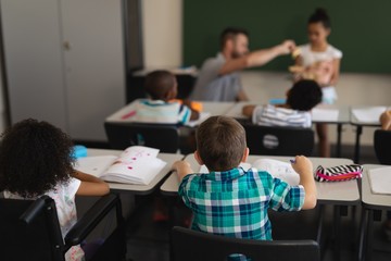 Rear view of schoolkids studying and sitting at desk in