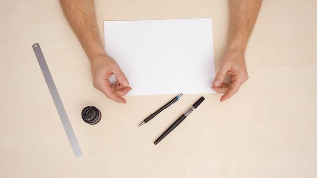 Mans hands on calligraphic desk. Close shot. Top view. White blanks, ruler, two brush pens on beige background. Arm position on designers workplace. Man laying his hands on beige desk. Lettering