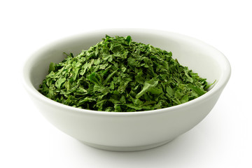 Dried chopped parsley in white ceramic bowl isolated on white.