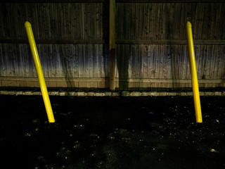 two yellow poles in front of a wooden fence at night