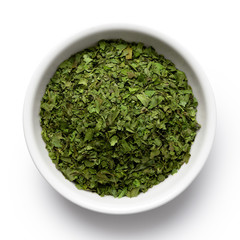 Dried chopped coriander leaves in white ceramic bowl isolated on white from above.