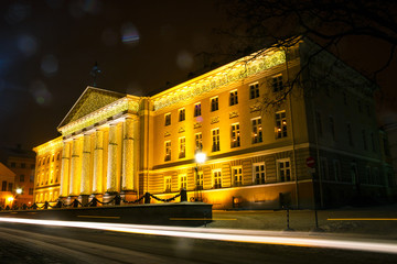 Facade of the main building of the University of Tartu, Estonia, in the Christmas decor on a winter evening. Trace from the car in the foreground.
