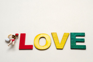 Obraz premium Love word made with colorful wooden letters and decorated with a little cupid against white background