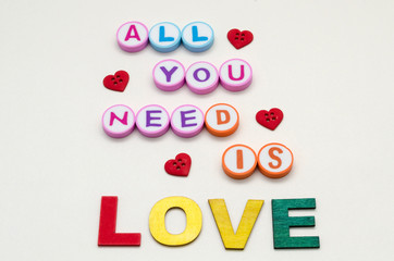 All you need is love phrase made with colorful letters made of wood and erasers and little red heart shape buttons against white background