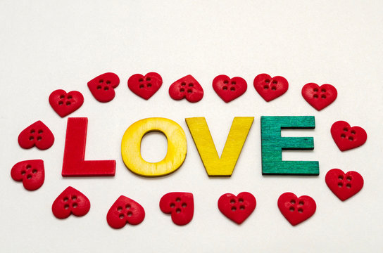 Love word made with colorful wooden letters and decorated with little red heart shape buttons against white background