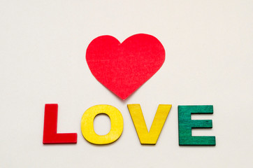 Love, word written with colorful wooden letters and a red paper heart against white background