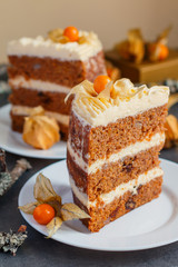 Two slices of homemade carrot cake with nuts, pears and cream-cheese and physalis as decoration on the plates with a small gift box on the background