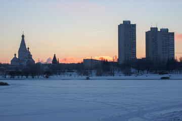 Fototapeta premium bright winter morning. bright scarlet sun rises on the horizon because of the houses and the Church. frosty clear weather on the street. smoke or steam from the pipes of factories