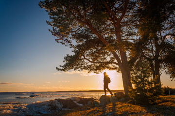 Young man stand under the tree on the lake shore during sunset in wintertime in south Estonia near Peipsi lake