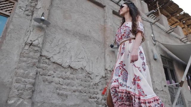 A beautiful European girl smiles and walks next to a renovated old Arab house. Lighting lamps and outdoor cameras mounted on the wall of the building