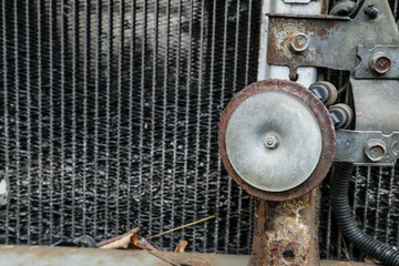 A detail of the old car wreck. The dirty radiator full of mess with a stone inside and the rusty horn are visible. 