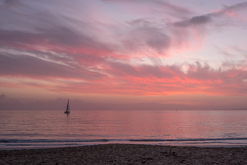 Colorful skies after Mallorcan sunset; sailboat on pink sea