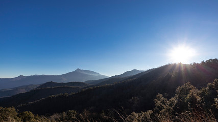 Sun shining over a solid blue sky on a mountain landscape