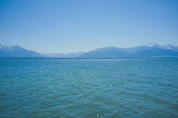Blick über den sommerlichen Chiemsee in Richtung der Alpen mit blauem Himmel