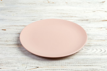 Perspective view. Empty pink matte plate on white wooden background