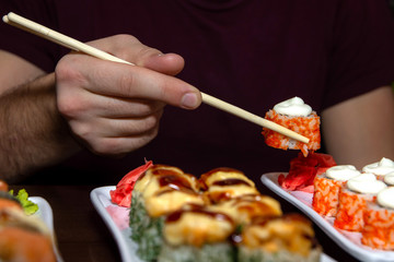 closeup man eating delicious sushi with chopsticks with food in the background