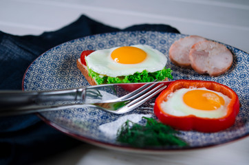 Sandwich with egg, ham, cheese, toast and salad leaves lies on a plate with tomato and dill