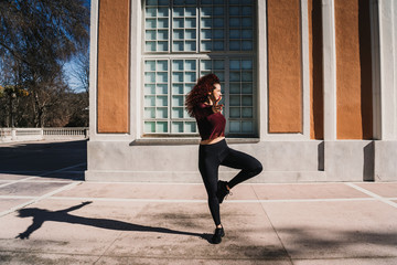 .Young beautiful latin woman with red curly hair doing exercise outdoors on a sunny winter day. Molding her body to be in good shape. Wearing sport wear. Lifestyle.